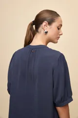 Blusa de manga corta color negro, con calce relajado, escote redondo con abertura y lazo para anudar. Presenta detalles de tablas horizontales en la parte superior que aportan textura al diseño.