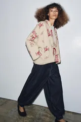 Chaqueta acolchada color beige con bordados florales en tonos rosados y rojos. Tiene escote en pico, manga larga y forro interior rojo. El cierre frontal es con alamar y tiene ribetes rojos.