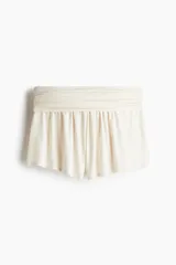 Short de color crema claro, confeccionado en tejido acanalado fino de viscosa. Presenta una cintura ancha con efecto fruncido o drapeado y un corte holgado.