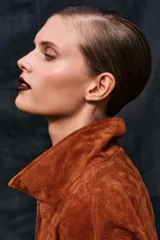 Cazadora de piel color marrón gamuzado, con cuello subido, manga larga, bolsillos delanteros con cierre de cremallera y cierre frontal metálico.