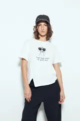 Remera blanca de manga corta con estampa frontal de un personaje con lentes de sol y la frase "Llegué tarde porque no quería venir". Tiene silueta relajada y calce cómodo, con un corte asimétrico en el bajo.