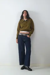 Sweater de punto color verde oliva, con cuello polo y cierre frontal parcial, de manga larga con puños anchos y diseño acanalado en el bajo.