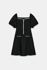 Vestido corto de tejido bouclé en color negro, con escote recto y mangas cortas abullonadas. Presenta detalles de vivos en color blanco a contraste en el escote, el centro del delantero y en los falsos bolsillos frontales.