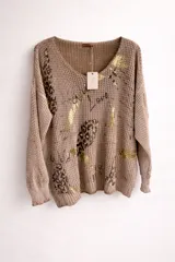 Buzo de tejido de punto abierto color beige, con diseño holgado, cuello redondo y mangas largas con puños acanalados. Presenta un estampado artístico que combina motivos de animal print y detalles brillantes en color dorado.