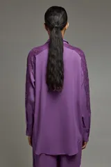 Camisa color lila confeccionada en crepe con encaje en hombros y mangas. Tiene cuello con lazo del mismo tono que se puede usar atado o suelto, escote en V, calce oversize y puños con botones personalizados a tono.