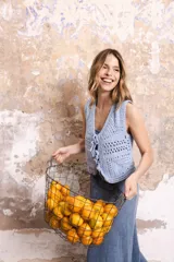 Chaleco corto tejido a mano en crochet, color celeste, con silueta ajustada, sin mangas y lazos en la delantera.