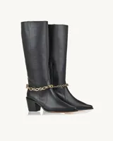 Bota alta de cuero negro con punta fina, taco geométrico y detalle de cadena dorada en el tobillo.