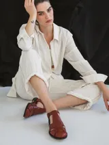 Sandalia cerrada tipo pescador, color blanco o hueso brillante, con tiras entrecruzadas en el empeine y cierre de hebilla ajustable en el lateral. Posee suela y taco bajo de color negro.