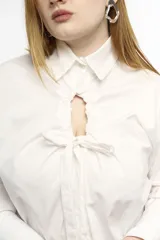 Camisa oversize de manga larga en color blanco, confeccionada en algodón. Presenta cuello clásico, puños abotonados y una abertura central ovalada con jaretas ajustables que permiten fruncir la prenda.