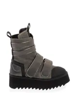 Bota tipo aviador de color gris con detalles en negro y tiras ajustables con velcro. Presenta una suela de plataforma gruesa con diseño dentado y puntera reforzada en negro.