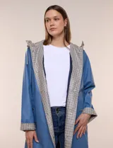 Pilot engomado impermeable color azul, de corte recto estilo trench con acabado resistente al agua. Cuenta con capucha integrada, cierre frontal con broches a presión, bolsillos laterales con ojal y forro interior de tela estampada a cuadros visible en la solapa y los puños.
