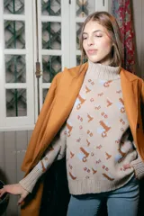 Polera de tejido de punto con cuello alto, diseño holgado y estampado jacquard con motivos geométricos y figuras en tonos beige, naranja y celeste.