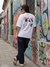 Remera blanca de algodón con corte oversize y estampado en la espalda de una playa con palmeras y una silla de playa.