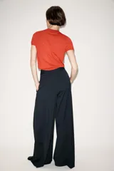 Pantalón de tiro medio con diseño wide leg, confeccionado en tejido con viscosa. Presenta un patrón de rayas diplomáticas, bolsillos laterales ocultos y detalle de pinzas pronunciadas en el delantero. Cierre frontal con cremallera, botón y ganchos metálicos.