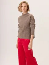 Buzo de lana color beige claro, con cuello chimenea y manga larga. Presenta trenzas de punto grueso en el frente y en los puños, con un diseño texturizado que se asemeja a espigas o ramas.