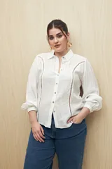 Camisa blanca de manga larga con cuello clásico y botones de nácar. Presenta detalles calados en el frente.