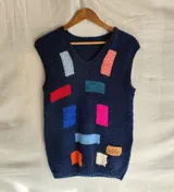 Chaleco tejido a mano de lana merino color azul marino, con cuello en V y diseño de rectángulos multicolores en el frente. Cuenta con una etiqueta de cuero con la marca en la parte inferior.