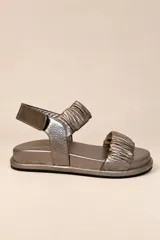 Sandalias de cuero color plateado, con dos tiras delanteras fruncidas, suela baja y tira en el talón con cierre de velcro.