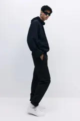 Pantalón cargo negro de nylon, corte recto y holgado, con cintura elástica y cordón ajustable. Presenta bolsillos cargo grandes en las piernas, bolsillos laterales y traseros con cierre, y cordón ajustable en los bajos.