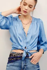 Camisa de poliéster color celeste, de manga larga abullonada con puños elastizados, escote en V con botones frontales y detalle fruncido en los hombros.