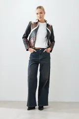 Chaqueta corta de cuero sintético color negro, marrón y blanco, con cuello de piel sintética blanca, cierre frontal con cremallera y bordado en las mangas.