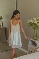 Camisón corto de satén color crema con escote en V y ruedo decorados con puntilla elastizada. Presenta breteles finos y espalda recta.