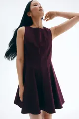 Vestido corto color borgoña, sin mangas, con escote redondo, costuras moldeadoras en el frente y la espalda, cierre oculto en la espalda y falda con vuelo.