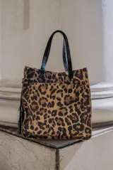 Bolso tipo tote bag con estampado animal print y asas cortas de charol negro. Incluye bolsillo exterior y llavero.