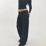 Jeans negros de tiro bajo y corte wide leg, con diseño de tachas metálicas plateadas a lo largo de las costuras laterales y delanteras.