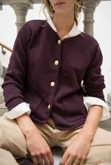 Cardigan de punto color beige con cuello redondo, cierre frontal con botones dorados, bolsillos frontales y terminaciones en crochet. Presenta hombreras internas y diseño de corte recto.