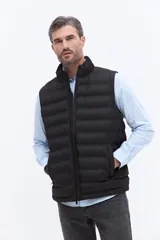 Chaleco puffer negro con diseño acolchado horizontal, cuello alto y cierre frontal. Presenta un bolsillo lateral con detalle de marca grabado.