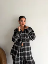 Camisa de corte oversize confeccionada en viyela, con estampado de cuadros en tonos negro, gris y blanco. Presenta cuello clásico, cierre frontal con botones, mangas largas con puños abotonados y bolsillos frontales.