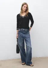 Jersey de punto fino de manga larga en color negro, con cuello en V y detalles de líneas blancas en contraste en el cuello y los puños.