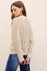 Sweater tejido de punto color beige con motas multicolor, cuello redondo y diseño de trenzas, de manga larga.