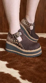 Guillerminas de cuero color chocolate, con plataforma corrida y suela alta a rayas. Presentan detalles en animal print de leopardo y acabado texturizado dorado en el talón, con tira ajustable y hebilla metálica.