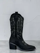 Bota texana de caña media en color negro, confeccionada en material tipo gamuza. Presenta bordados decorativos en hilo blanco y detalles de tachas metálicas en la caña, con taco cuadrado y punta estilizada.