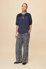 Blusa de manga corta color negro, con calce relajado, escote redondo con abertura y lazo para anudar. Presenta detalles de tablas horizontales en la parte superior que aportan textura al diseño.