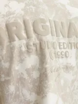 Camiseta de manga corta y cuello redondo, con fit oversize. Presenta un estampado tipo tie-dye o acid wash en tonos beige y crema.