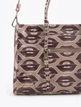 Bandolera de cuero vacuno con estampado de labios, manijas de mano y correa ajustable para llevar al hombro o cruzada. Cuenta con un bolsillo frontal con cierre y un llavero colgante con dije de corazón.