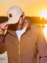 Gorra unisex de color beige con visera curva y aplique de cuero con logo grabado en el frente. Cuenta con hebilla metálica posterior para ajuste.