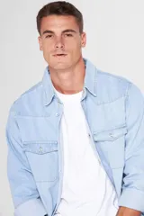 Camisa de jean celeste de manga larga, con cuello clásico, cierre frontal con botones a presión, dos bolsillos con solapa abotonada en el pecho, corte en hombros y detalle en la espalda.