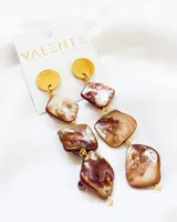 Aros colgantes con base circular dorada y tres piedras irregulares nacaradas en tonos marrones y blancos, unidas por argollas doradas.