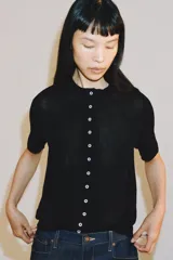 Chaqueta de punto fino color negro, con cuello redondo, manga corta y cierre frontal con múltiples botones a contratono.