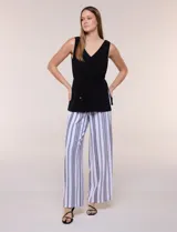 Enterito de efecto dos piezas con parte superior negra lisa, escote en V y sin mangas, y parte inferior de pantalón palazzo de corte amplio con diseño a rayas en blanco y negro. Cuenta con cintura entallada con lazo ajustable.