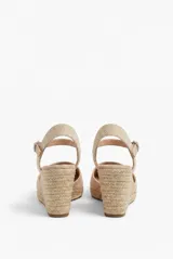 Sandalia de plataforma con cuña de yute y suela texturizada, color beige. Cuenta con puntera cerrada, diseño destalonado y tira ajustable al tobillo con hebilla metálica.