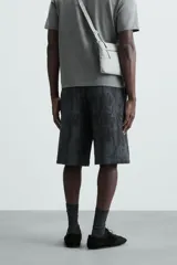 Bermuda de corte relajado, color gris oscuro con efecto tie-dye o textura irregular. Presenta cintura elástica ajustable con cordón y bolsillos laterales y traseros de plastrón.