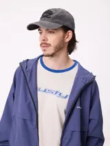 Gorra gris oscuro con efecto desgastado, visera curva con detalles rotos y logotipo bordado en relieve en el frente.