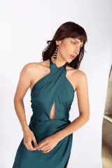 Vestido largo verde petróleo de seda lavada, con escote halter cruzado, abertura en el abdomen, falda con capas y flecos.