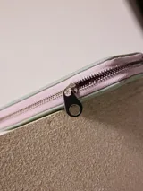 Billetera de poliuretano texturizado color rosado con cierre perimetral y logo metálico al frente.