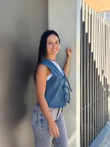 Chaleco de jean azul con cierre frontal mediante lazos ajustables, sin mangas y corte recto.